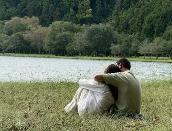 A couple resting by a lake on a work-for-accommodation summer break, recharging in the UK countryside