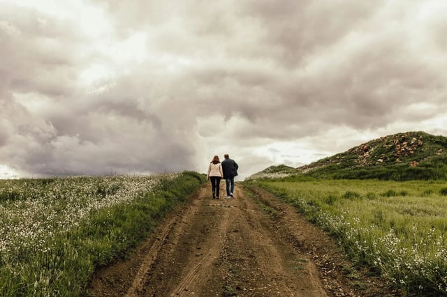 A couple walk a quiet country path under cloudy skies, reflecting the calm of off-peak season hosting.