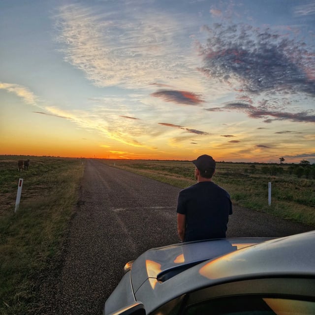 Traveller watching the sunset from a country road